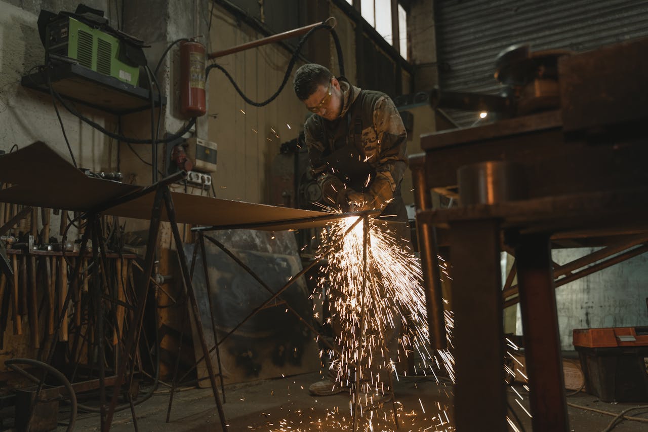 about-img-01 Male welder in safety gear welding metal with sparks in an industrial setting.
